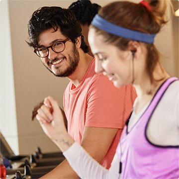 Rapaz sorrindo e moça na esteira da academia